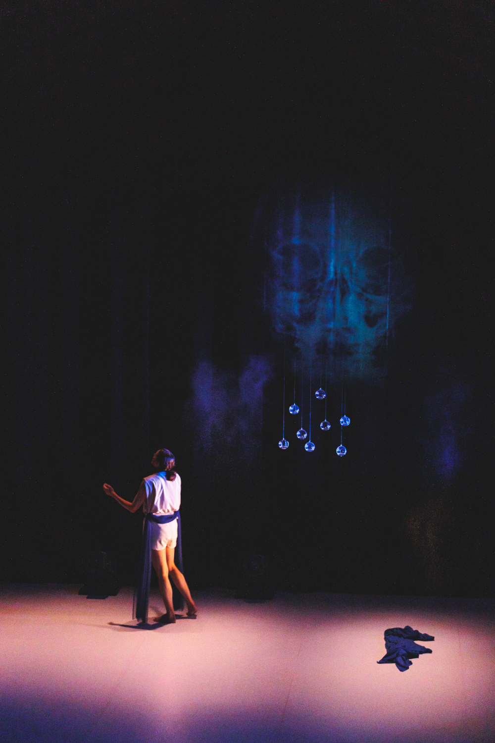 La danseuse Lea Anderson cherche un fantôme dans une lumière douce et un crâne bleu apparaît au loin, création lumière de Jérôme Baudouin, créateur lumière en danse, théâtre et spectacle vivant